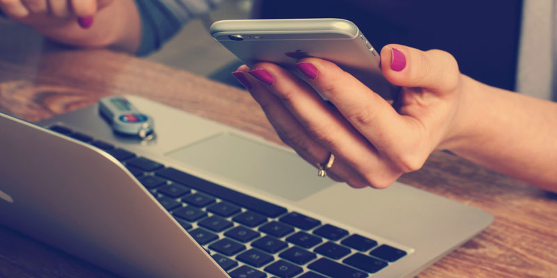 woman holding phone and sitting in front of laptop