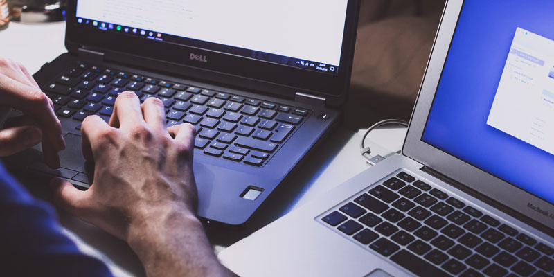 user with two laptops on desk