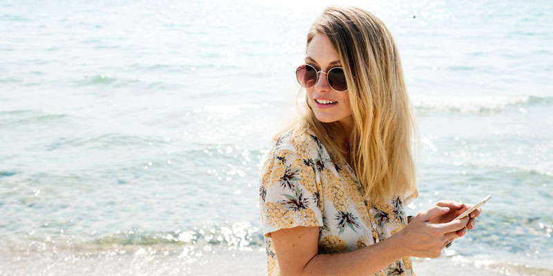 woman at beach on a sunny day looking away from smartphone in hand