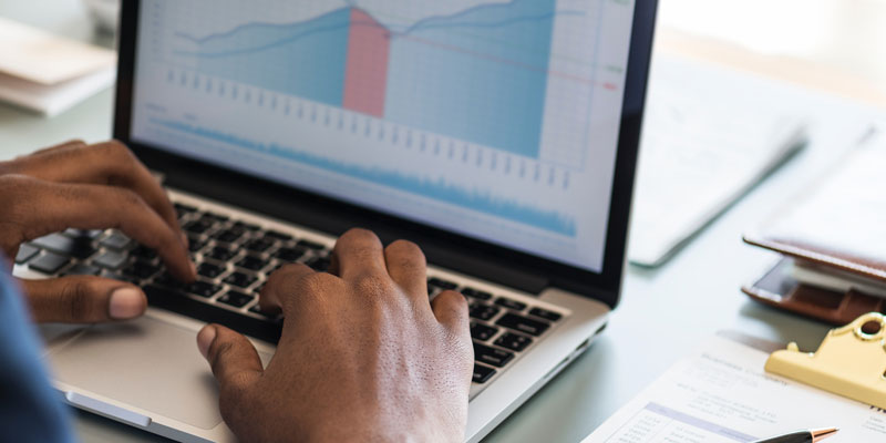 close-up of man's hands using laptop with line graph on screen