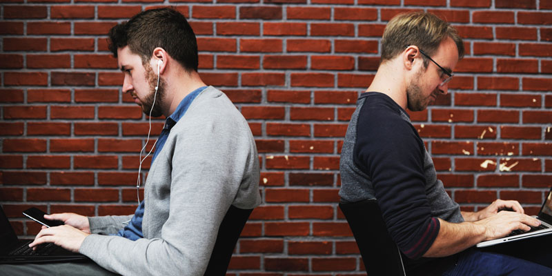 two men working back-to-back outside with a brick wall background