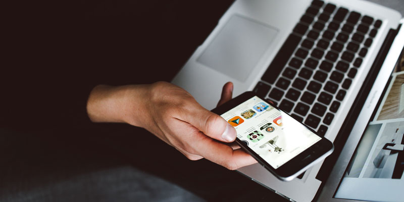 person holding smartphone and using laptop