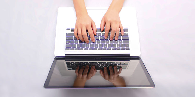 hands typing on laptop with reflection on screen